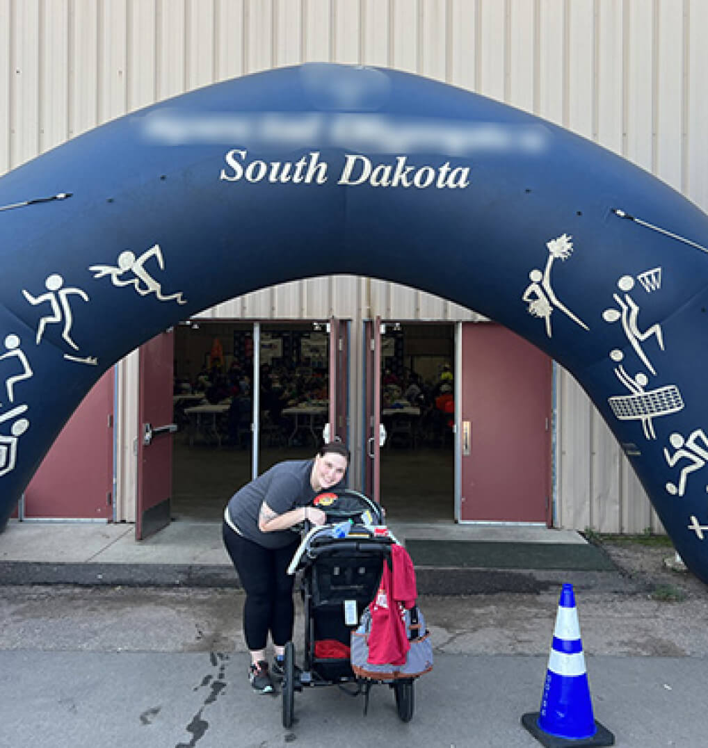 Woman posing with a stroller under a Special Olympics arch