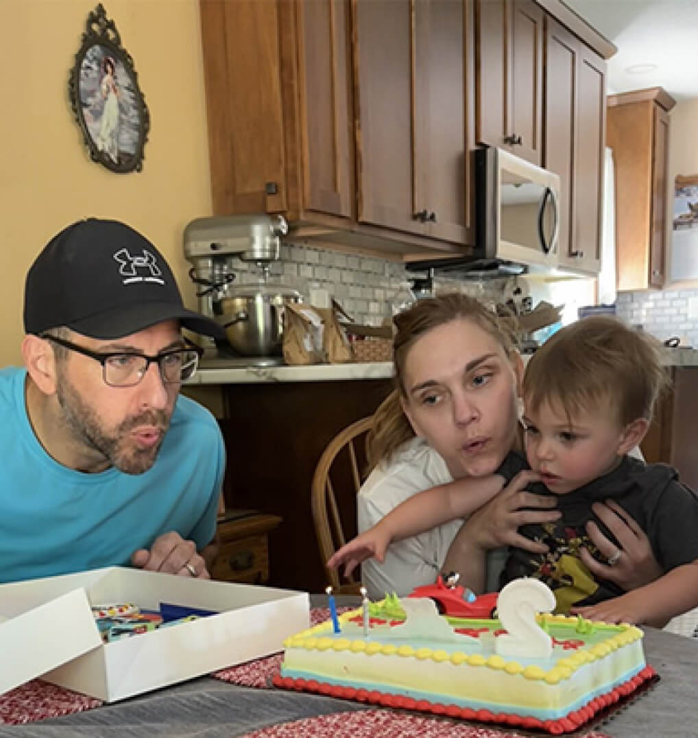 Two parents helping their son blow out a birthday candle 